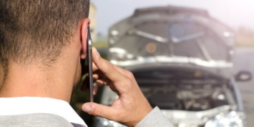 Man standing by the broken vehicle calling tow service.