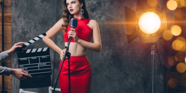 young stylish sexy woman on cinema backstage, celebrating, red satin evening dress, party mood, luxury style, fashion trend, singing in vintage microphone, bokeh