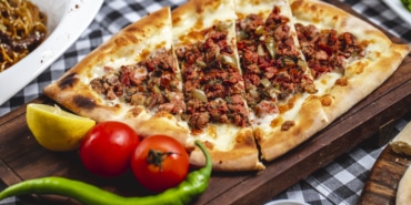 side view pide bread with ground meat tomato hor green pepper cheese and slice of lemon on a board