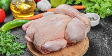 Raw whole chicken with lettuce, peppers, spices and tomatoes on wooden plate