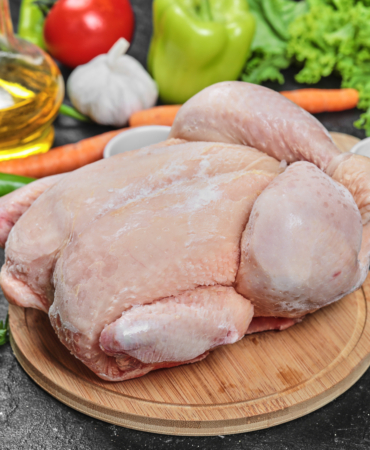 Raw whole chicken with lettuce, peppers, spices and tomatoes on wooden plate