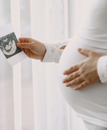 Pregnant woman stands by the window and looks at photo