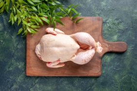 top-view-fresh-chicken-with-green-leaves-dark-blue-surface