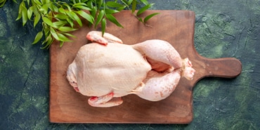 top-view-fresh-chicken-with-green-leaves-dark-blue-surface