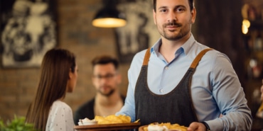 Portrait of smiling waiter serving food in a pub.